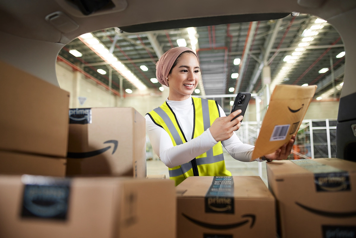 Amazon delivery driver in safety vest scanning packages with phone in fulfillment center