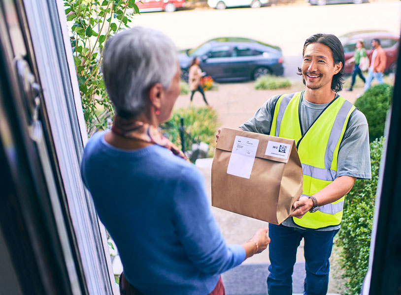 Delivery driver in safety vest handing package to customer at their home in residential neighborhood setting
