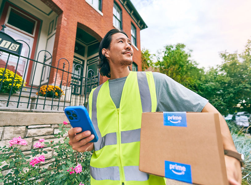 Amazon Prime delivery person in reflective vest holding package and phone outside residential building