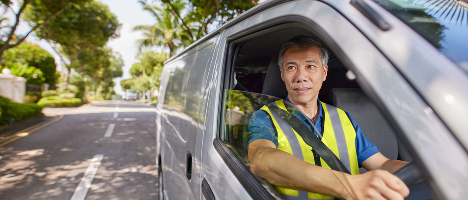Man in yellow vest driving a van on a tree-lined street